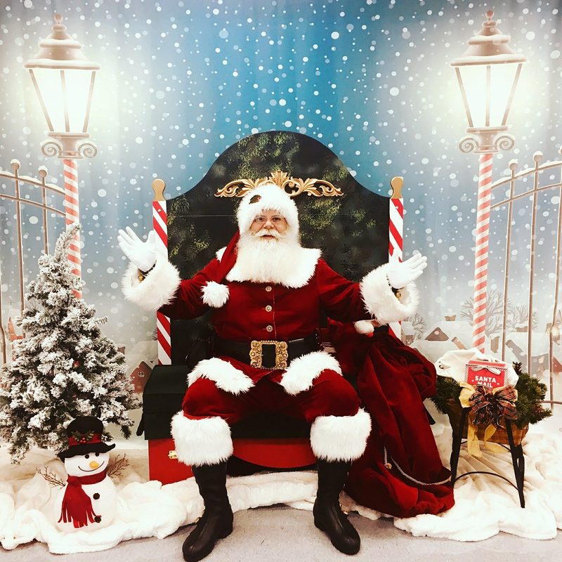 Santa Claus seated on his own chair between two lampposts.
