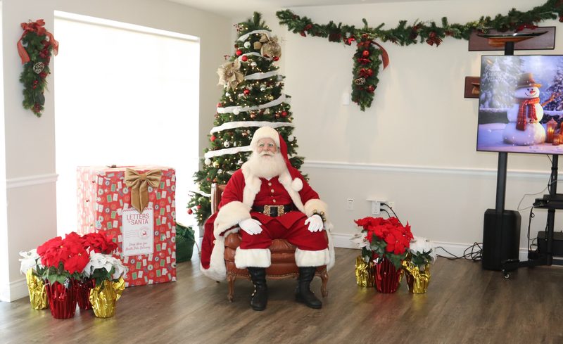Santa Claus at a decorated venue beside a Christmas tree.